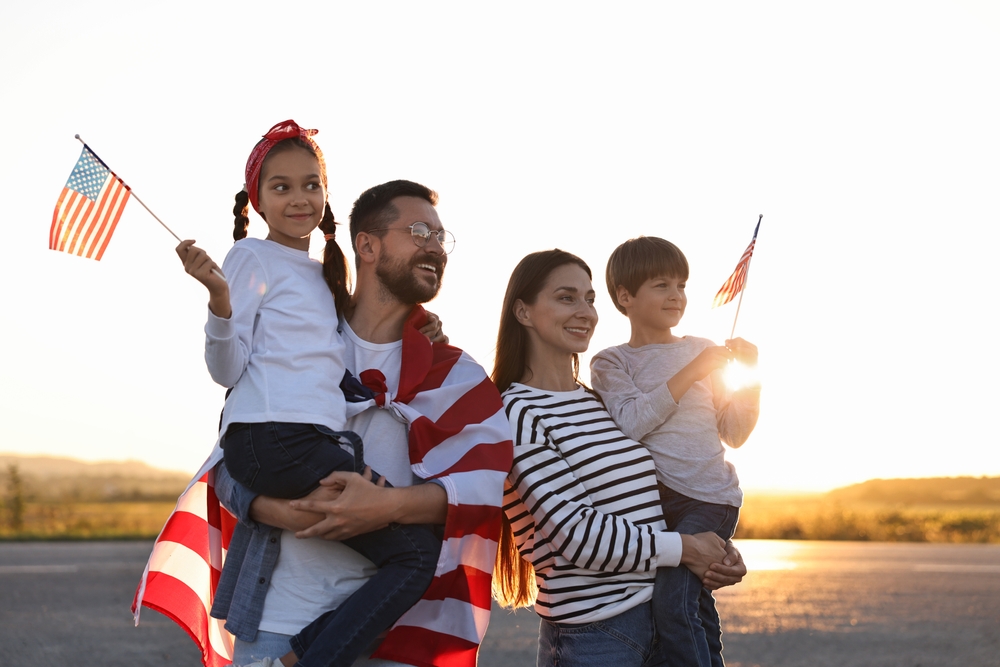 Family holding American flags outdoors at sunset